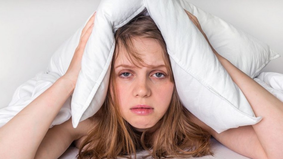 Mujer con una almohada en la cabeza. con problemas para dormir