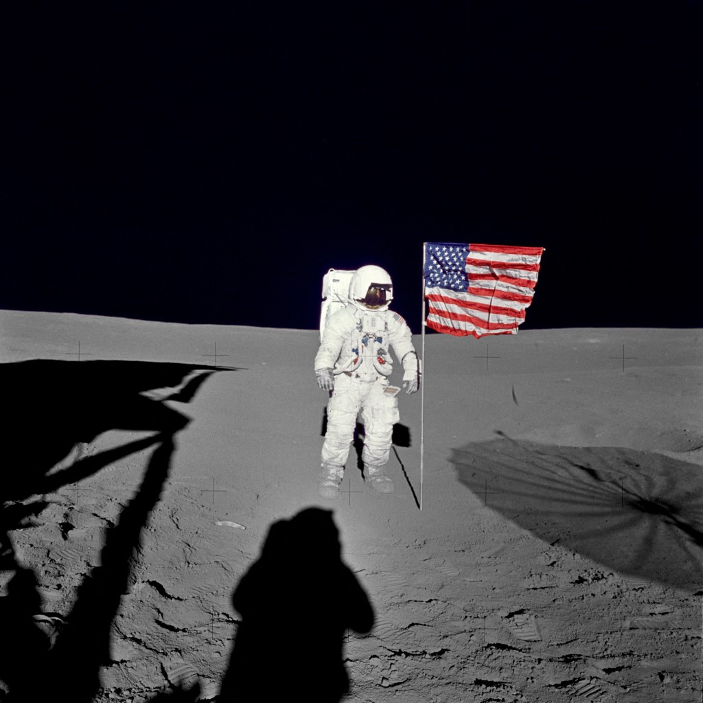 Edgar Mitchell junto a la bandera estadounidense flameando sobre superficie lunar.