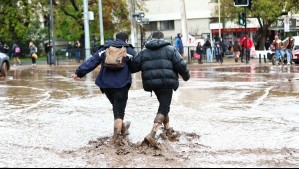 Personas cruzando por una calle inundada en Las Condes.